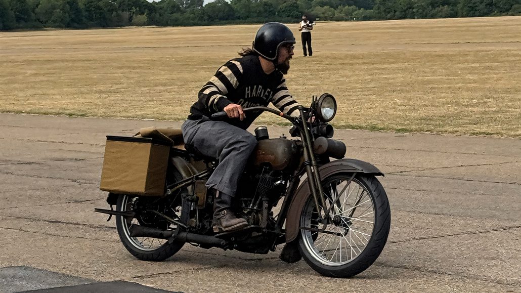 Jason Momoas 1920er-Harley wird zum Plug-in-Hybrid: Technik im Detail 1 Jason Momoa fährt Harley-Davidson Model JD Plug-in-Hybrid auf Flugplatz – Harley-Davidson Pullover mit Streifen, schwarzer Helm, Canvastasche am Heck
