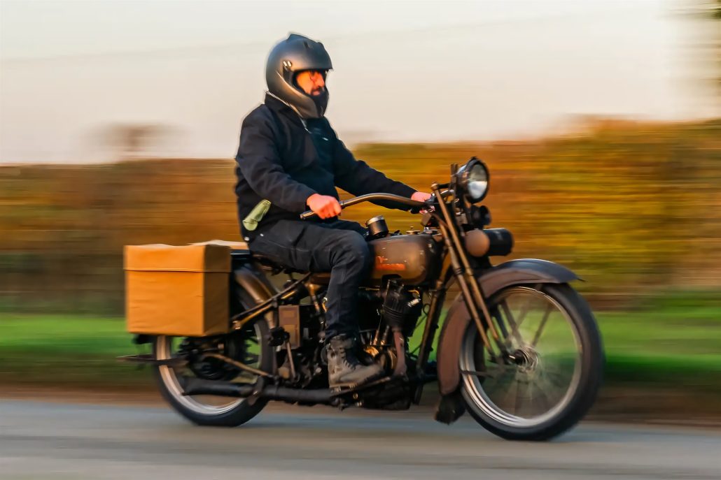 Jason Momoas 1920er-Harley wird zum Plug-in-Hybrid: Technik im Detail 4 Fahrer auf Harley-Davidson Model JD Plug-in-Hybrid bei Geschwindigkeit – Panning-Aufnahme mit herbstlicher Landschaft, schwarze Motorradkleidung, Canvastasche am Heck