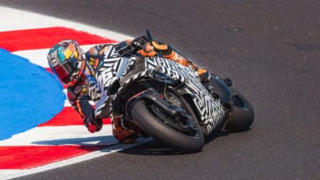 KTM 850 MotoGP Testmotorrad 2026 – Schräglage in der Kurve mit schwarz-weißer Dazzle-Tarnung, Arai-Helm und orangefarbenen Handschuhen auf der Rennstrecke von Misano mit rot-weiß-blauen Kerbs