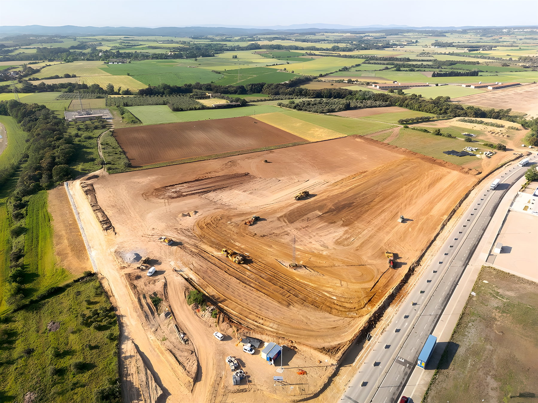 Rieju Werk Vilamalla – Luftbild der Großbaustelle mit schwerem Gerät und Erdarbeiten, grüne Landschaft und Pyrenäen-Ausläufer im Hintergrund