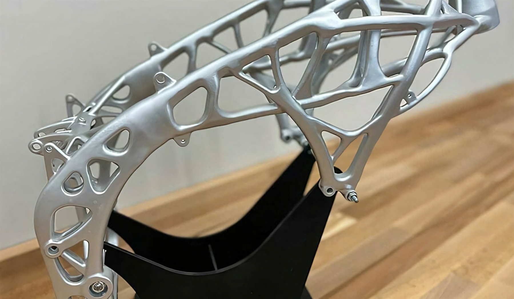 3D-gedruckter Motorradrahmen aus Aluminium mit topologieoptimierter Gitterstruktur auf schwarzem Ständer im Studio – Beispiel für additive Fertigung im Fahrzeugbau