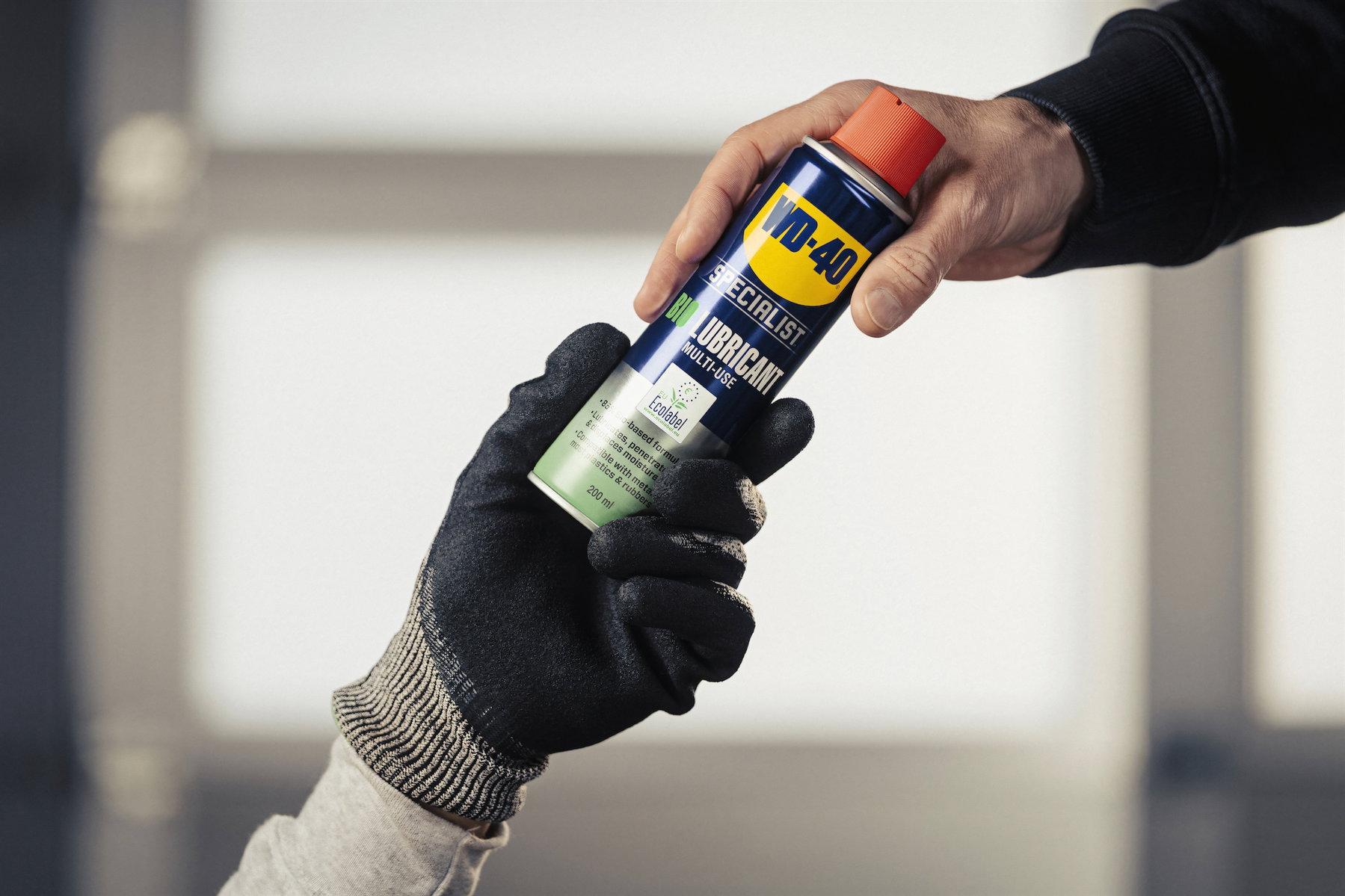 Eine Hand reicht die WD-40 Specialist Bio-Schmierspray Dose an eine Person mit schwarzem, schnittfestem Arbeitshandschuh weiter
