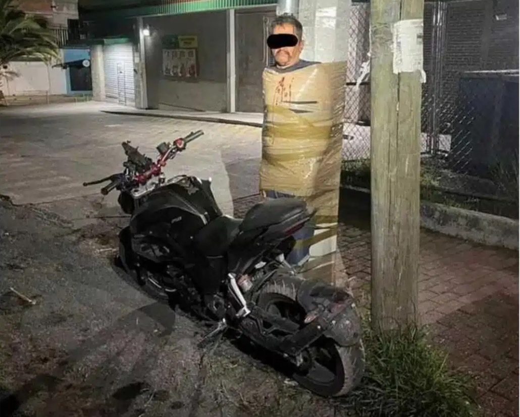 Mexikos Batman klebt Motorraddiebe an Masten: Behörden ermitteln 1 Mutmasslicher Motorraddieb mit Klebeband an einen Strommast gefesselt neben einem schwarzen Motorrad bei Nacht in Lagos de Moreno Mexiko
