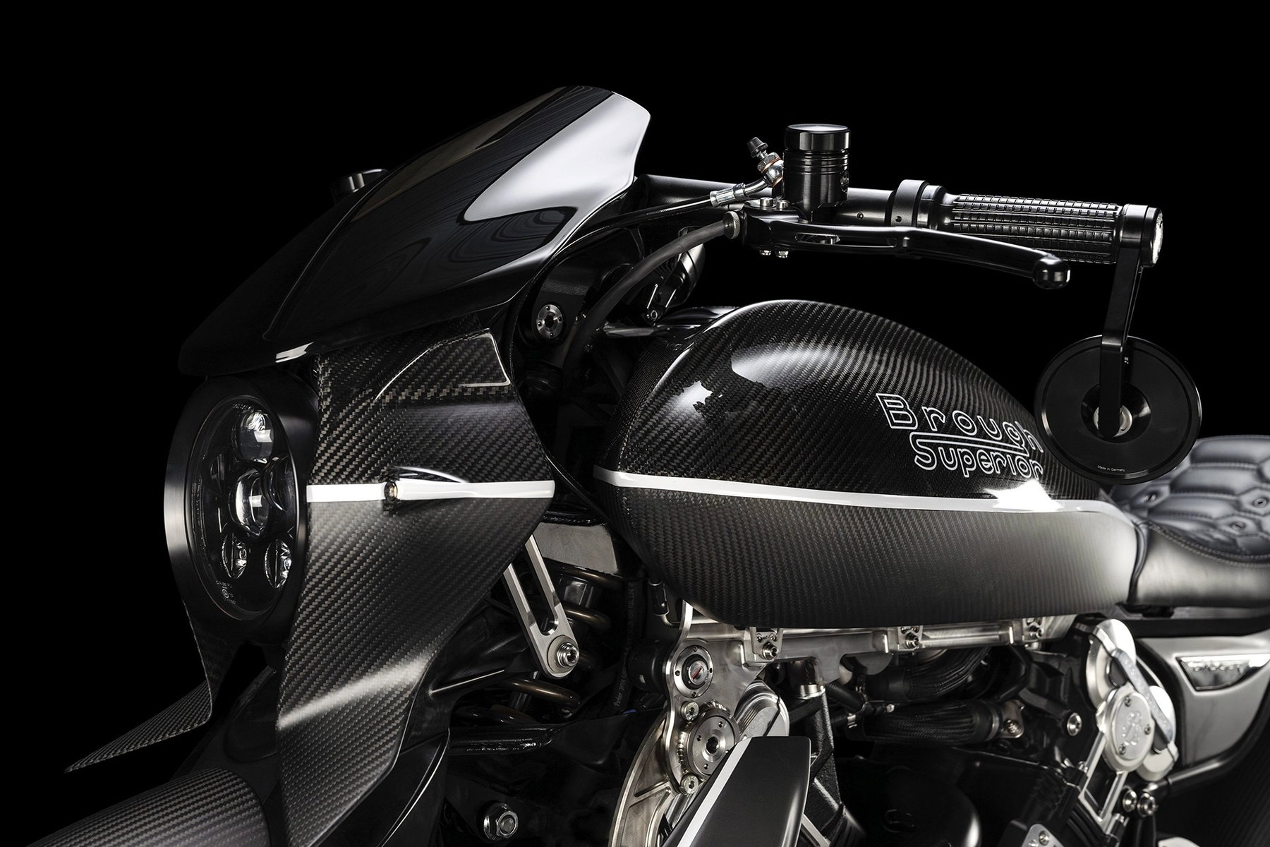 Brough Superior Dagger S: Was die neue Sportvariante wirklich ändert 5 Brough Superior Dagger S 2026 – Detailansicht Frontpartie und Tank im Studio, Carbon-Verkleidung mit sichtbarer Gewebestruktur, getönte Windschutzscheibe, Brough Superior Logo auf dem Tank, CNC-gefräster Tankdeckel