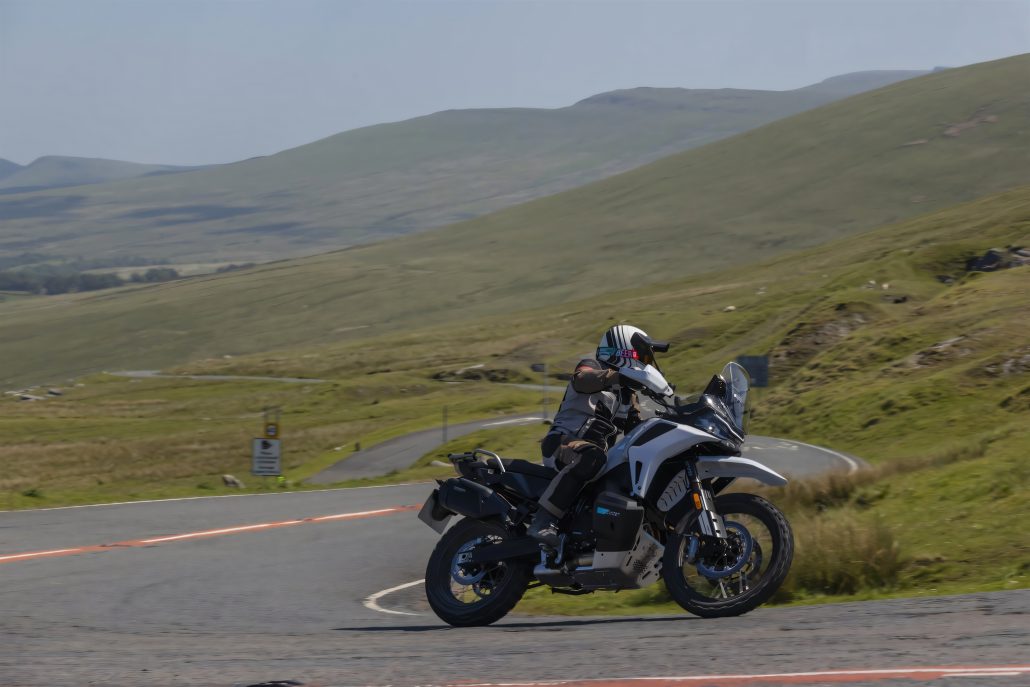 Brembo und CFMoto: Warum Europas Zulieferer jetzt China stärken 6 CFMoto 1000 MT-X Adventure-Motorrad in Schräglage auf kurviger Bergstraße mit Fahrer in Reiseausrüstung, im Hintergrund grüne Hügellandschaft