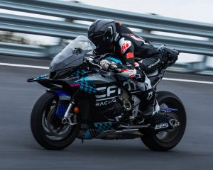 CFMoto V4SR-RR Prototyp in türkis-schwarzer CFMoto-Racing-Lackierung in Schräglage auf der Rennstrecke, Fahrer mit chinesischer Flagge am Ärmel, Startnummer 85