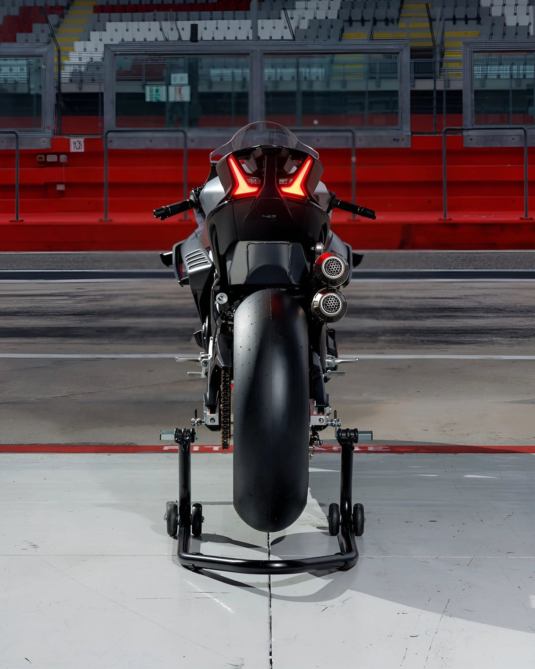 CFMoto V4SR-RR Prototyp von hinten auf der Boxengasse vor roter Tribüne, LED-Rücklicht, runde Doppelauspuffendtöpfe, auf Montageständern abgestellt