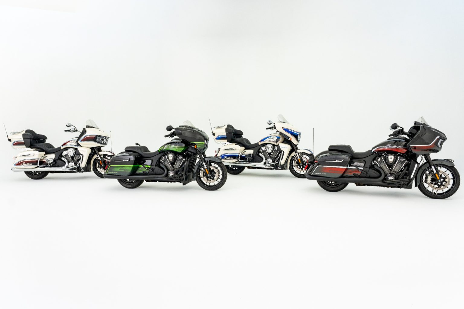Hochauflösendes Gruppenfoto aller vier Indian PowerPlus Signature Series Modelle 2026 im Fotostudio: Roadmaster PowerPlus in Frontier Pearl mit Revere Red/Vigilant Blue (links), Chieftain PowerPlus in Abyss Metallic mit Venom Green/Cypher Green, Indian Pursuit in Frontier Pearl mit Revere Red/Vigilant Blue und Indian Challenger in Abyss Metallic mit Machined Silver/Red Alert (rechts)