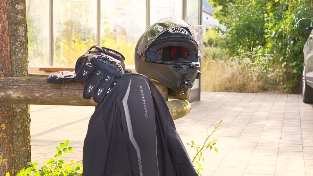 Kemimoto Motorradjacke und Handschuhe 2026 – Jacke über einem Holzzaun, daneben die Handschuhe und ein schwarzer Integralhelm auf dem Zaunpfosten
