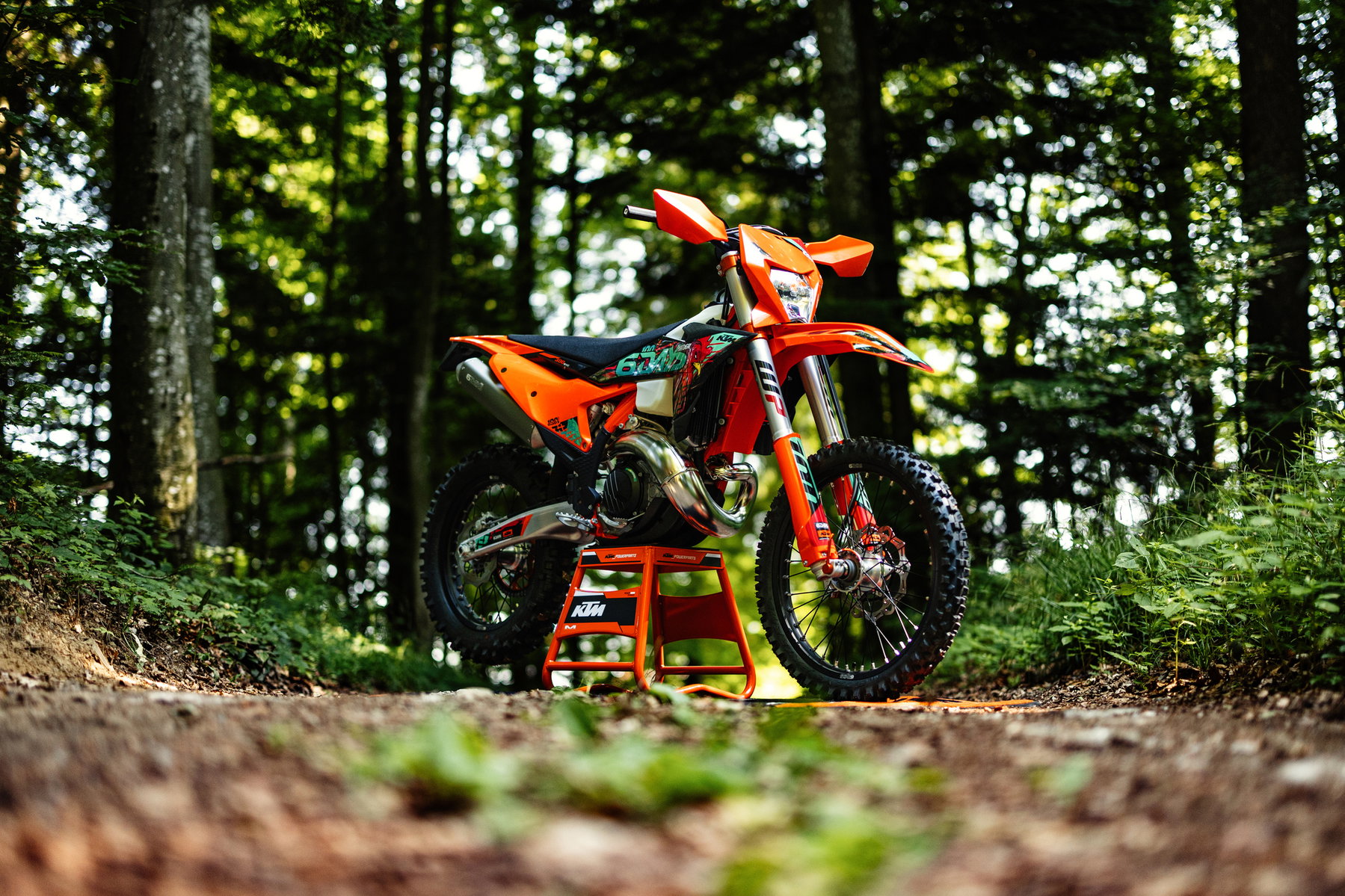 KTM EXC 6DAYS 2027: Special Edition for the 100th Six Days in Portugal 1 KTM 300 EXC 6DAYS 2027 – Enduro auf Montageständer auf einer Waldkuppe im Gegenlicht
