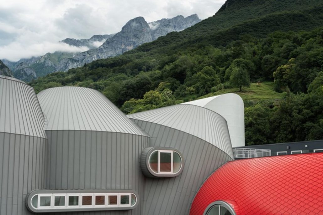 Moto Guzzi Opens New Factory: What's Changing in Mandello in 2026 1 Moto Guzzi World Days 2026 – close-up view of the curved gray and red roofs of the new factory building against a mountain backdrop