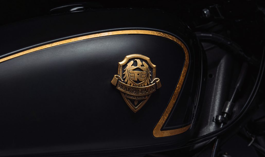 Royal Enfield Shotgun 650 x Rough Crafts – Tankdetail mit goldenem Zierstreifen und Messing-Wappenbadge Rough Crafts x Royal Enfield