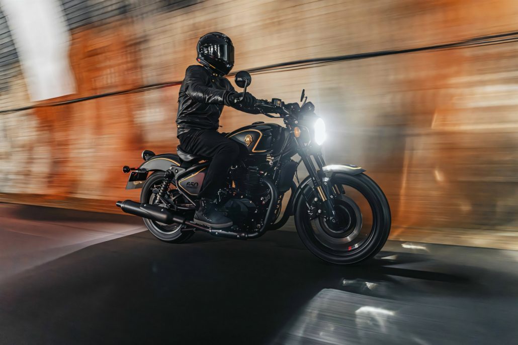 Royal Enfield Shotgun 650 x Rough Crafts – Fahraufnahme mit Bewegungsunschaerfe in orange beleuchtetem Tunnel, Fahrer in schwarzer Kombi