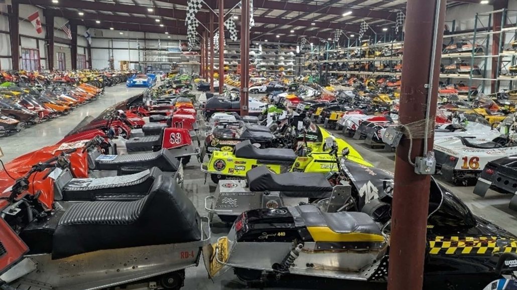 US Fraud Case: 600 Motorcycles and Snowmobiles Go Under the Hammer 1 Classic racing snowmobiles in red, yellow, black and white parked tightly together with race numbers and sponsor decals in a large warehouse