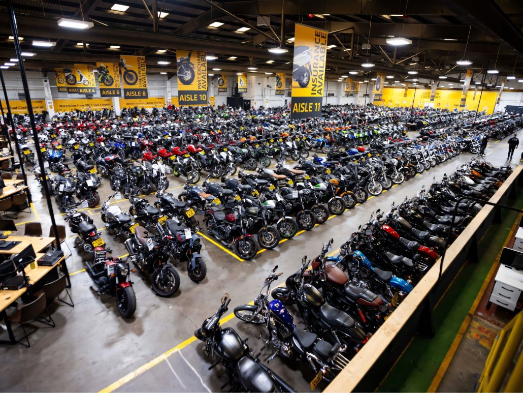SuperBike Factory ist insolvent: Das bedeutet es für Motorradfahrer 3 Luftaufnahme der riesigen SuperBike-Factory-Halle mit hunderten aufgereihten Gebrauchtmotorrädern in nummerierten Gängen unter gelben Werbebannern für Teilzahlung und Versicherung