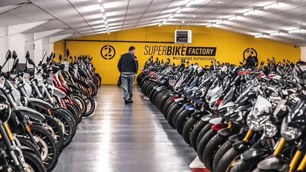 SuperBike Factory ist insolvent: Das bedeutet es für Motorradfahrer 5 Innenansicht einer SuperBike-Factory-Filiale mit gelber Wandbeschriftung 'Motorbike Superstore', ein Kunde geht zwischen zwei langen Reihen aufgereihter Gebrauchtmotorräder hindurch