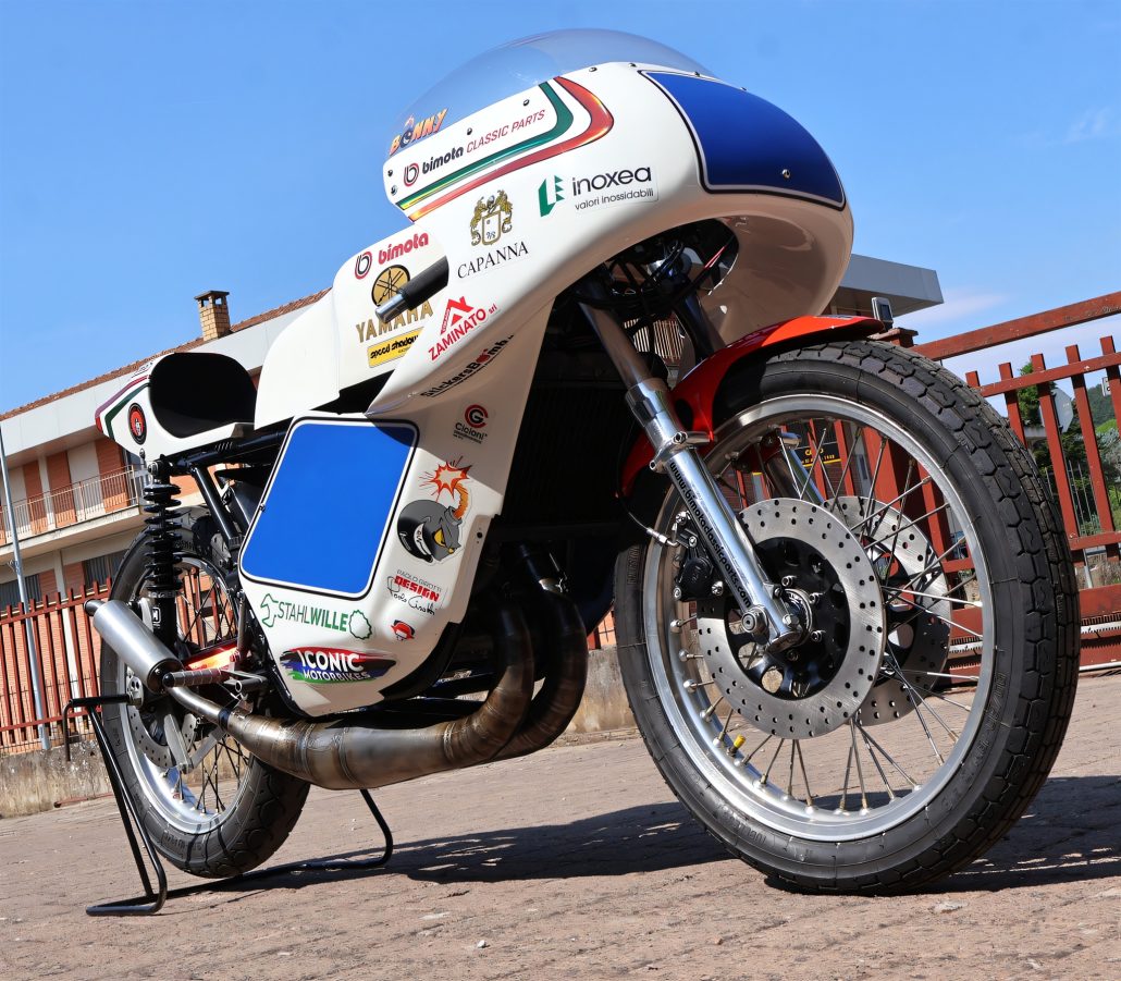 Yamaha/Bimota TZ 350 GP 2026 – Froschperspektive von vorn rechts mit Zweitakt-Auspuffkrümmern und Bimota-Classic-Parts-Verkleidung vor blauem Himmel
