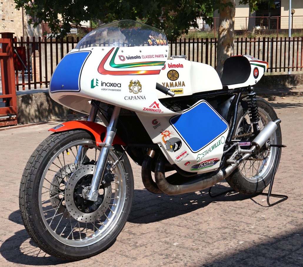 Yamaha/Bimota TZ 350 GP 2026 – Dreiviertelansicht von vorn links mit blau-weißer Verkleidung, rotem Frontkotflügel und Zweitakt-Krümmern