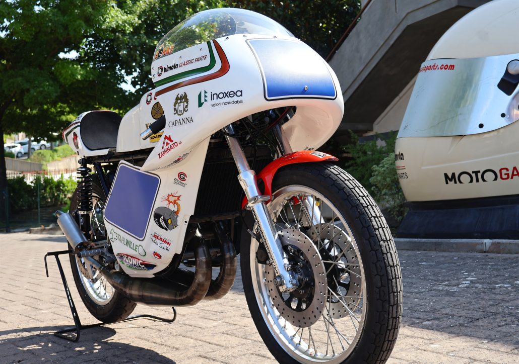 Yamaha/Bimota TZ 350 GP 2026 – Frontansicht aus niedriger Perspektive vor einer überdimensionalen Helm-Skulptur mit Bimota-Classic-Parts-Beschriftung