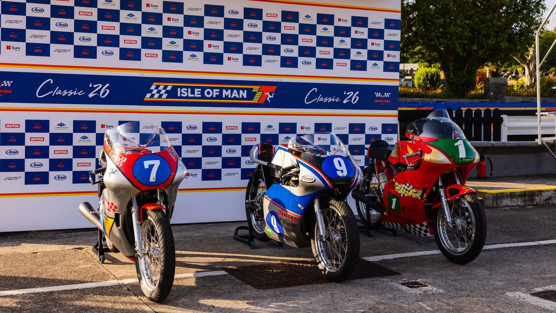 Die drei 350-cm³-Rennmaschinen der Podestplatzierten mit den Startnummern 7, 9 und 1 vor der Classic-26-Sponsorenwand – Historic Junior Classic TT, Isle of Man 2026