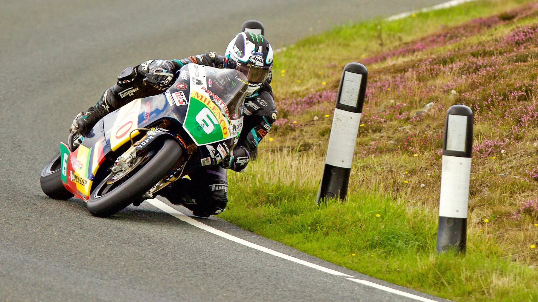 Classic TT: Dunlop Breaks the Anstey Record and Wins Twice in a Day 2 Michael Dunlop in tiefer Schräglage auf der Milenco-by-Padgetts-Honda mit der Startnummer 6 zwischen blühendem Heidekraut am Mountain Course – Lightweight Classic TT, Isle of Man 2026