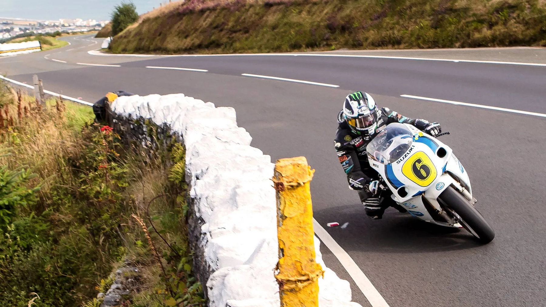 Michael Dunlop in tiefer Schräglage auf der Suzuki GSX-R750 von Team Classic Suzuki, Küstenlandschaft und weiße Steinmauer im Hintergrund – Senior Classic TT, Isle of Man 2026