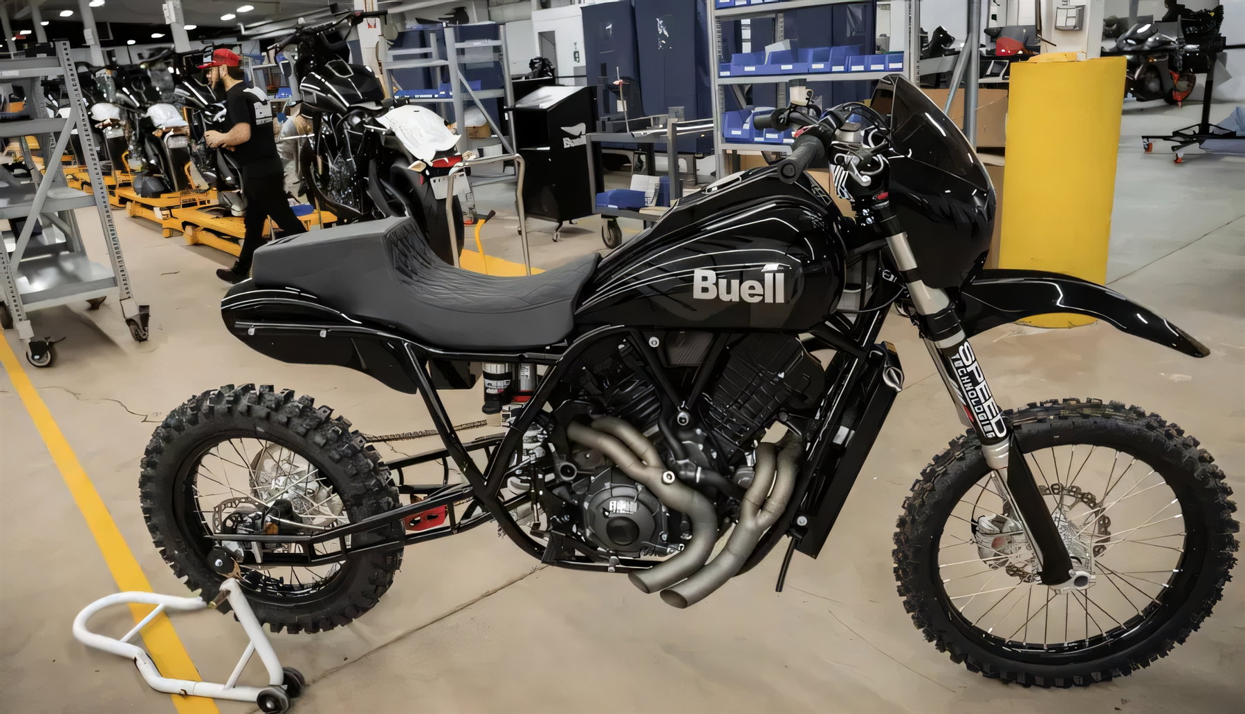 Buell The Goat Bergrenn-Konzept 2026 – Seitenansicht des kompletten Fahrzeugs in der Werkshalle, im Hintergrund weitere Motorräder und ein Mitarbeiter.