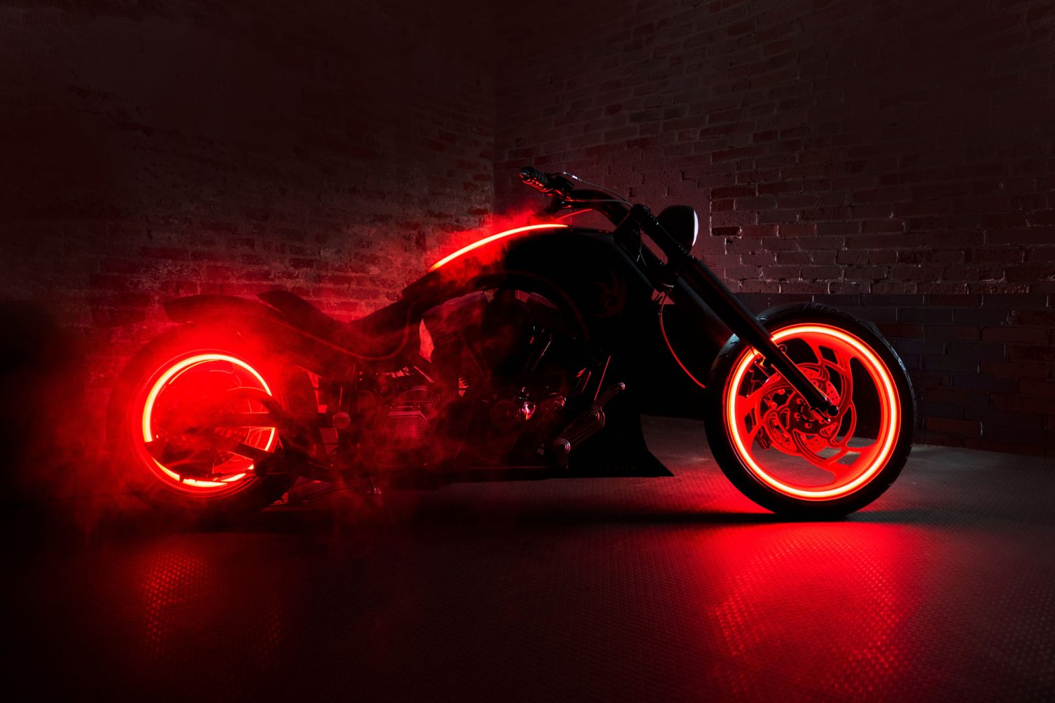 Sega spendet Dark Rider: Guintoli versteigert Sonic-Bike für Stiftung Dark Rider Custombike von Bourget's Bike Works in dramatischer Studioinszenierung mit rotem Rauch und Neonlicht, Seitenansicht vor dunkler Ziegelwand