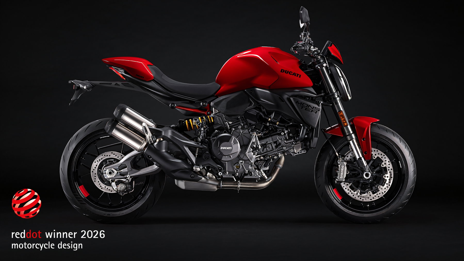 Ducati Monster 2026 in Ducati Red – Seitenansicht im Studio mit 890 cm³ V2, Aluminium-Zweiarmschwinge, Showa-Federbein und Brembo-Bremsanlage, daneben das Red Dot Winner 2026 Logo