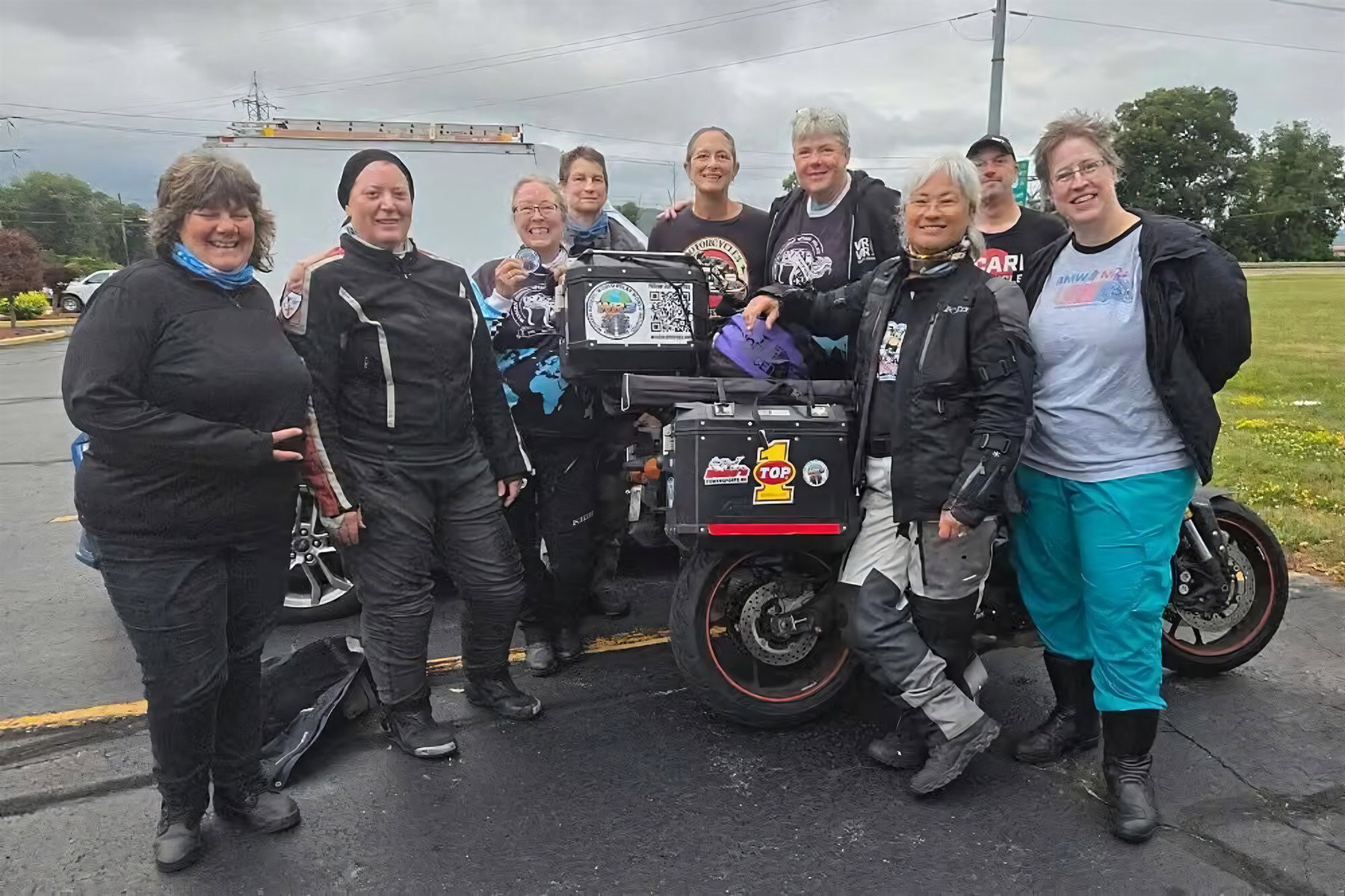 GPS-Zeichnung als Weltrekord: 21.860 Kilometer für vier Buchstaben 5 Gruppe von Motorradfahrerinnen und -fahrern in Regenmontur posiert gemeinsam mit einem bepackten Reisemotorrad