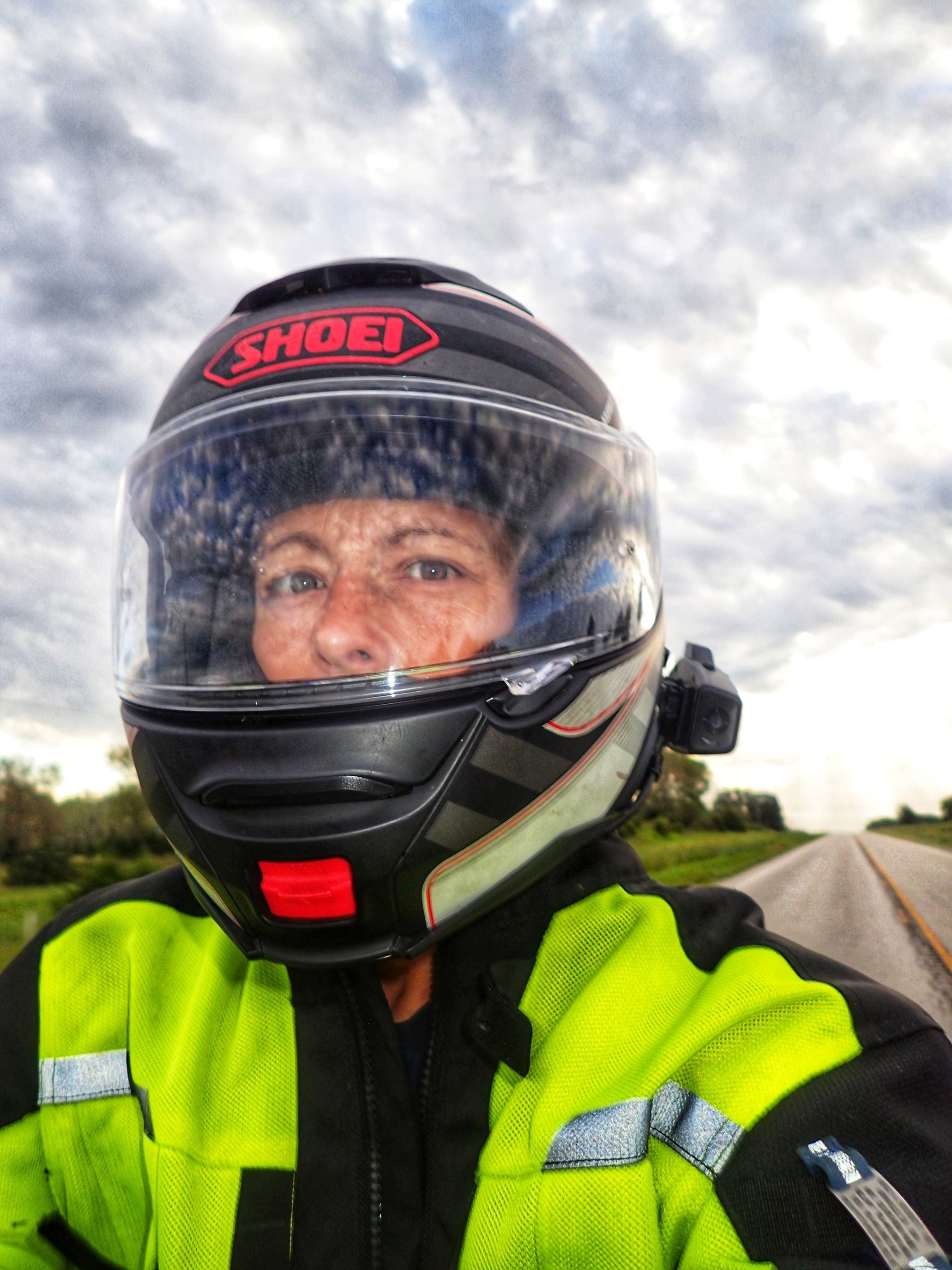 GPS-Zeichnung als Weltrekord: 21.860 Kilometer für vier Buchstaben 4 Nahaufnahme einer Motorradfahrerin mit Helm und neongelber Jacke auf einer leeren Landstraße unter bewölktem Himmel