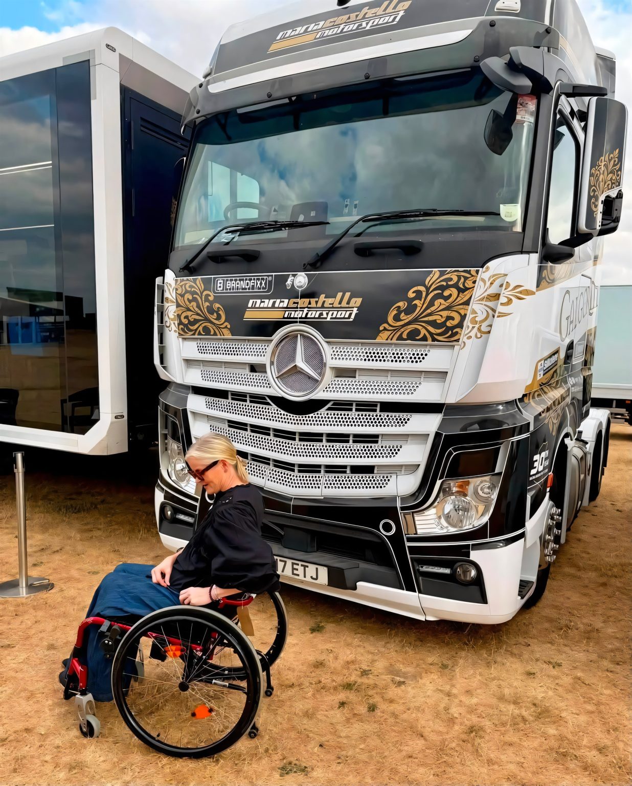 Maria Costello zurück im Fahrerlager: Was der Besuch in Thruxton bedeutet Maria Costello im Rollstuhl vor dem schwarz-weiß-goldenen Mercedes-Actros-Truck von Maria Costello Motorsport im Fahrerlager von Thruxton