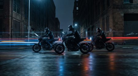 Drei Motorraeder fahren nachts durch eine enge Stadtstrasse auf nassem Asphalt