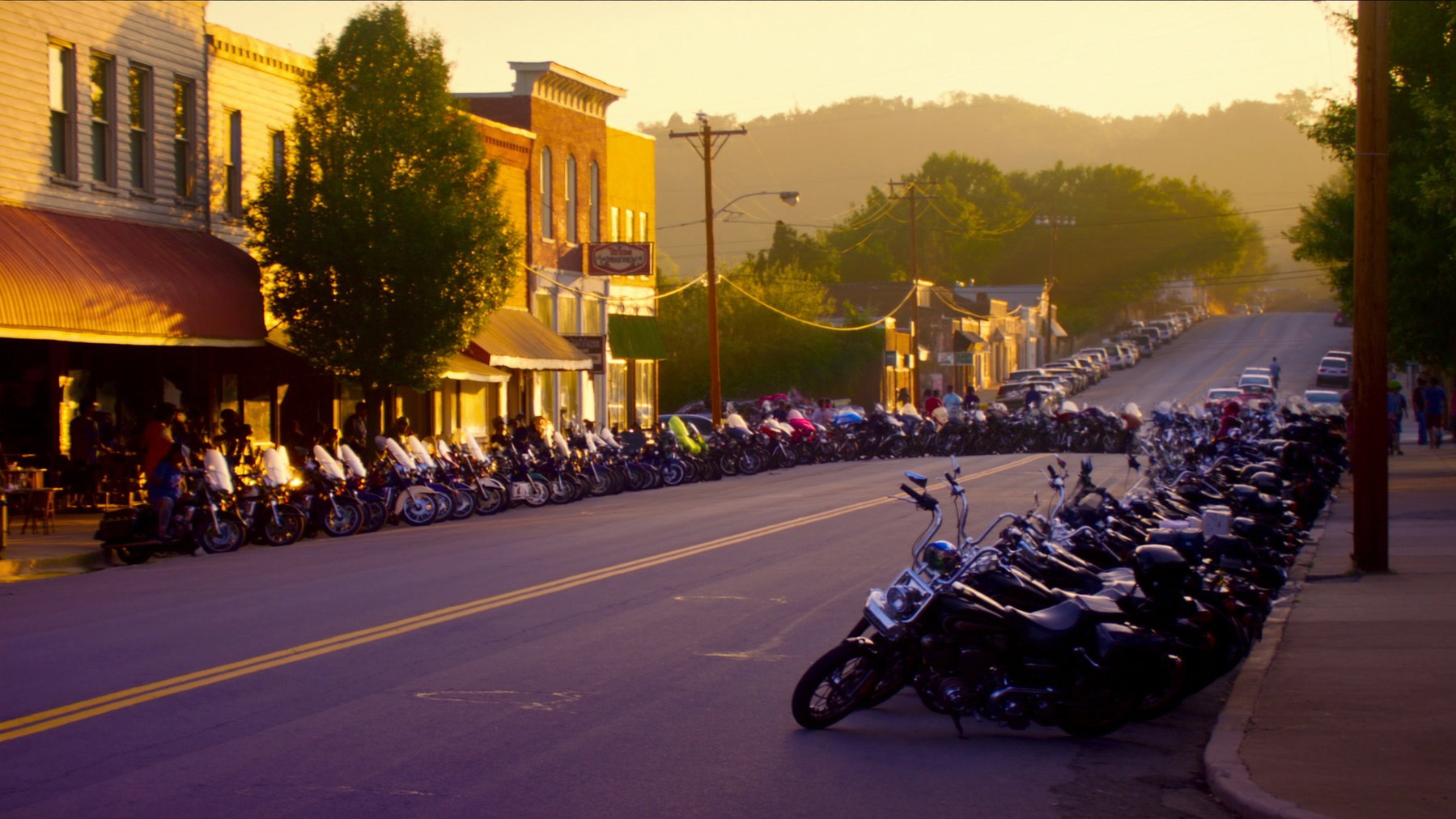 Sturgis Rally 2026: Crashes Down 25 Percent, Drug Offences Up Belebte Hauptstrasse einer amerikanischen Kleinstadt mit Reihen geparkter Motorraeder im warmen Abendlicht waehrend der Sturgis Motorcycle Rally