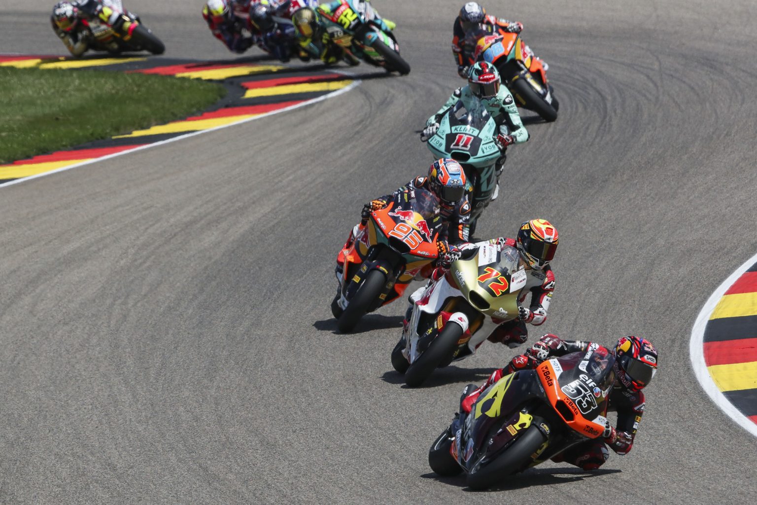 Moto2-Feld in Schräglage auf dem Sachsenring beim Deutschland-Grand-Prix 2026, angeführt von Deniz Öncü mit Startnummer 53 vor den Maschinen mit den Startnummern 72, 95 und 11 – alle angetrieben vom Triumph 765-cm³-Dreizylinder