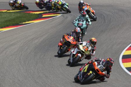 Moto2-Feld in Schräglage auf dem Sachsenring beim Deutschland-Grand-Prix 2026, angeführt von Deniz Öncü mit Startnummer 53 vor den Maschinen mit den Startnummern 72, 95 und 11 – alle angetrieben vom Triumph 765-cm³-Dreizylinder