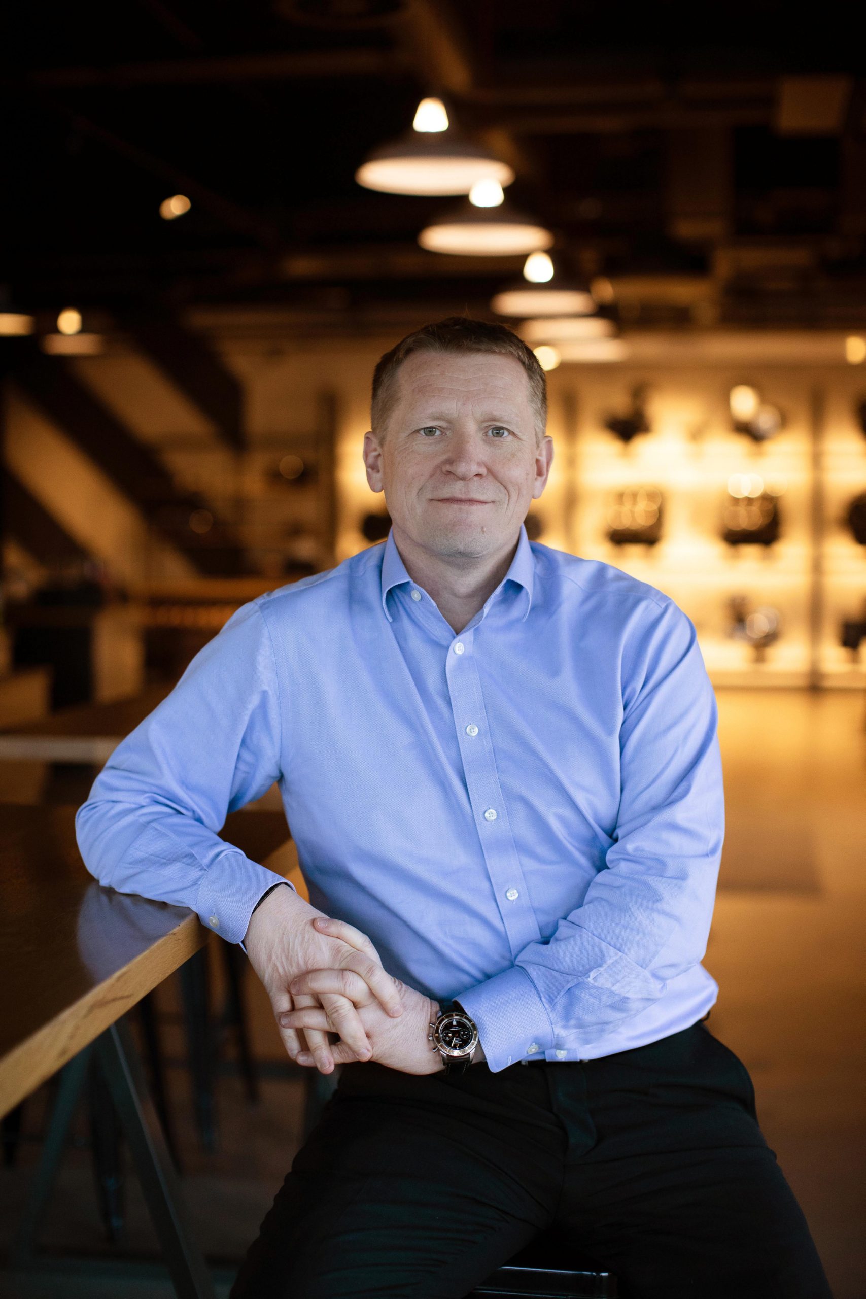 Triumph trennt Vertrieb und Marketing: BMW-UK-Chef George kommt 1 Paul Stroud, Chief Commercial Officer von Triumph Motorcycles, der 2026 in den Ruhestand geht – Porträt im hellblauen Hemd in einer Triumph-Ausstellungshalle