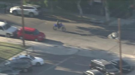 Luftaufnahme eines Dirtbike-Fahrers, der bei einer Polizeiverfolgungsjagd in Los Angeles zwischen Autos über eine breite Kreuzung fährt, die Person ist durch Verpixelung unkenntlich gemacht