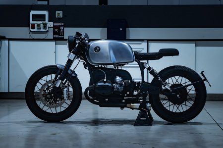 BMW R 100 Umbau von Bolt Motor Company, Seitenansicht Cafe-Racer-Stil mit gebuerstetem Aluminium-Tank gegen schwarz strukturierten Rahmen und Motorblock, in der Werkstatt fotografiert