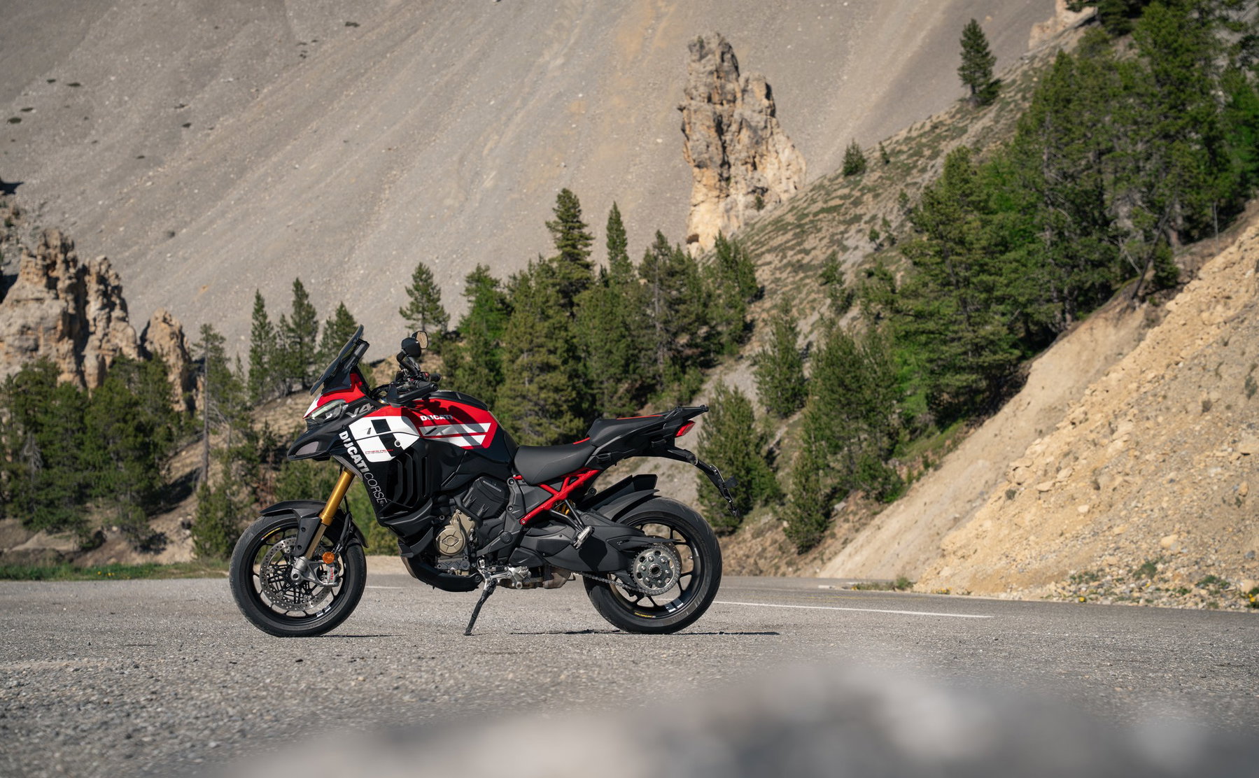 Ducati Multistrada V4 Pikes Peak 2027: MotoGP Look, Same Technology 4 Ducati Multistrada V4 Pikes Peak 2027 mit schwarzen Schmiederädern und neuer Lackierung in Rot, Weiß und Schwarz, linke Seitenansicht mit rotem Gitterrohr-Heckrahmen auf einer Passstraße im Gebirge