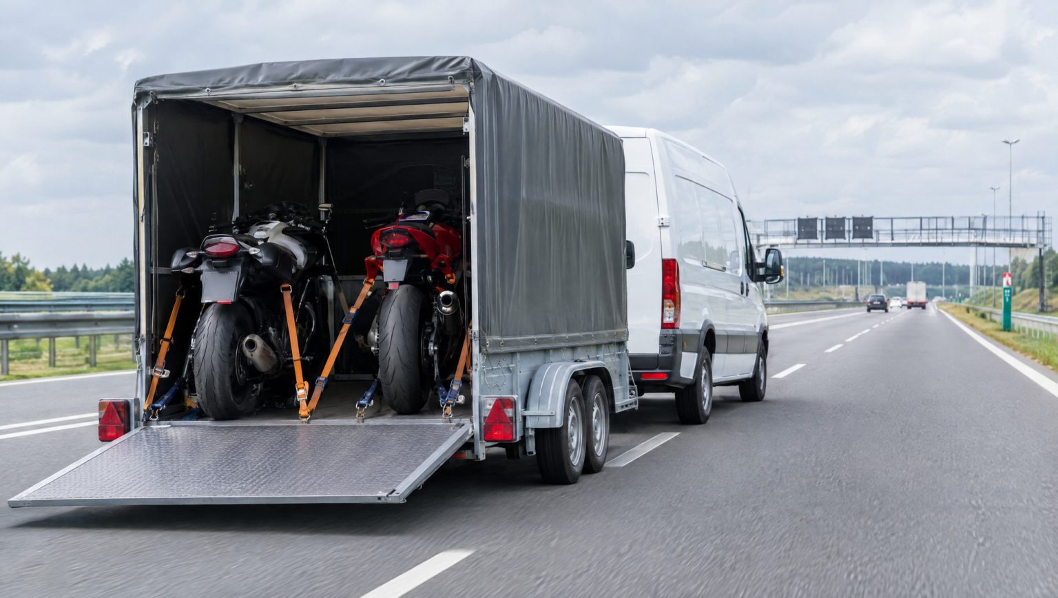 Poland scraps e-TOLL for trailers: credit only refundable until March 2027 Weißer Transporter zieht einen geschlossenen Anhänger mit zwei gesicherten Motorraedern auf einer polnischen Autobahn, Heckansicht mit heruntergelassener Laderampe