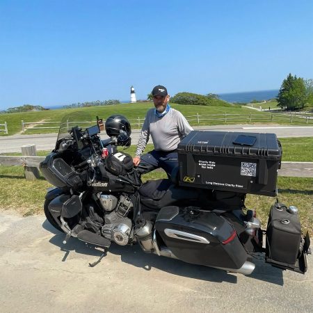 Indian Pursuit 2025 – Seitenansicht der schwarzen Tourenmaschine mit KLIM-Topcase, Zusatztank und PowerPlus-112-V2 vor einem Leuchtturm an der Atlantikküste