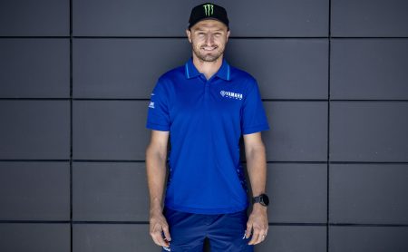 Jack Miller im blauen Yamaha-Racing-Polohemd und schwarzer Monster-Energy-Cap vor einer dunkelgrauen Paneelwand – Querformat-Ankündigungsbild zum Wechsel in die Superbike-WM 2027