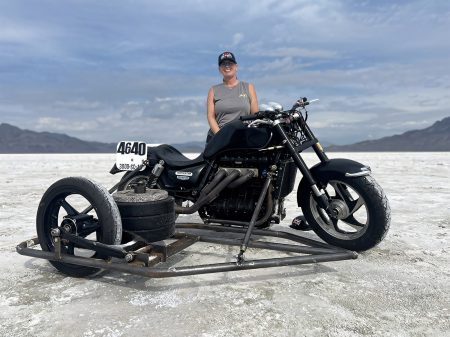 Liane Langlois steht laechelnd hinter ihrem schwarzen Triumph-Rocket-III-Dreirad-Renner mit Beiwagen-Gewicht auf der Salzpiste von Bonneville, Startnummer 4640
