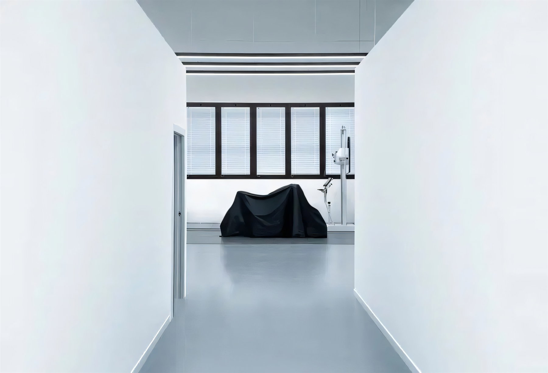 Modena40 wird 10: Warum CFMOTOs Zukunft in Italien entsteht 1 Minimalistischer weisser Flur im Designstudio von Modena40 in Rimini mit Blick auf ein unter schwarzem Tuch verdecktes Motorrad und Vermessungsequipment