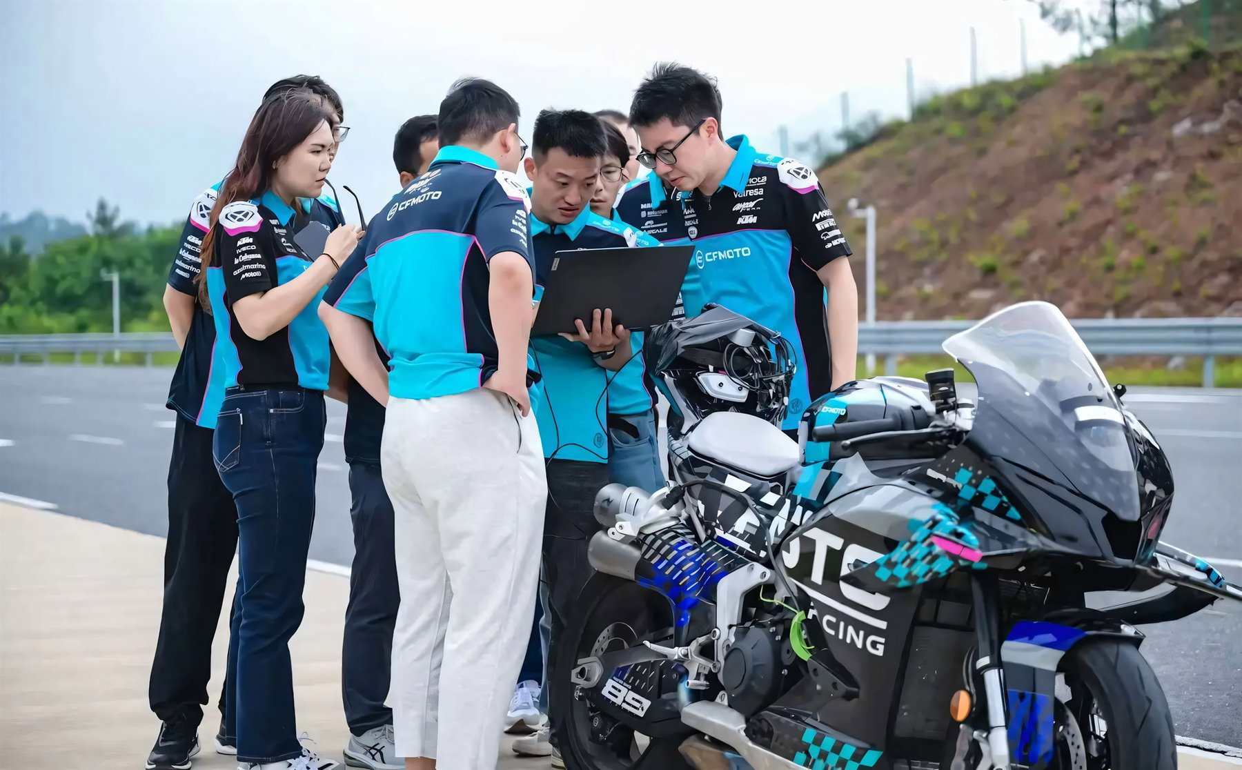 Modena40 wird 10: Warum CFMOTOs Zukunft in Italien entsteht 7 CFMOTO-Racing-Team in tuerkis-schwarzer Teambekleidung bespricht Telemetriedaten auf einem Laptop neben dem getarnten CFMOTO-Superbike-Prototyp auf einer Teststrecke