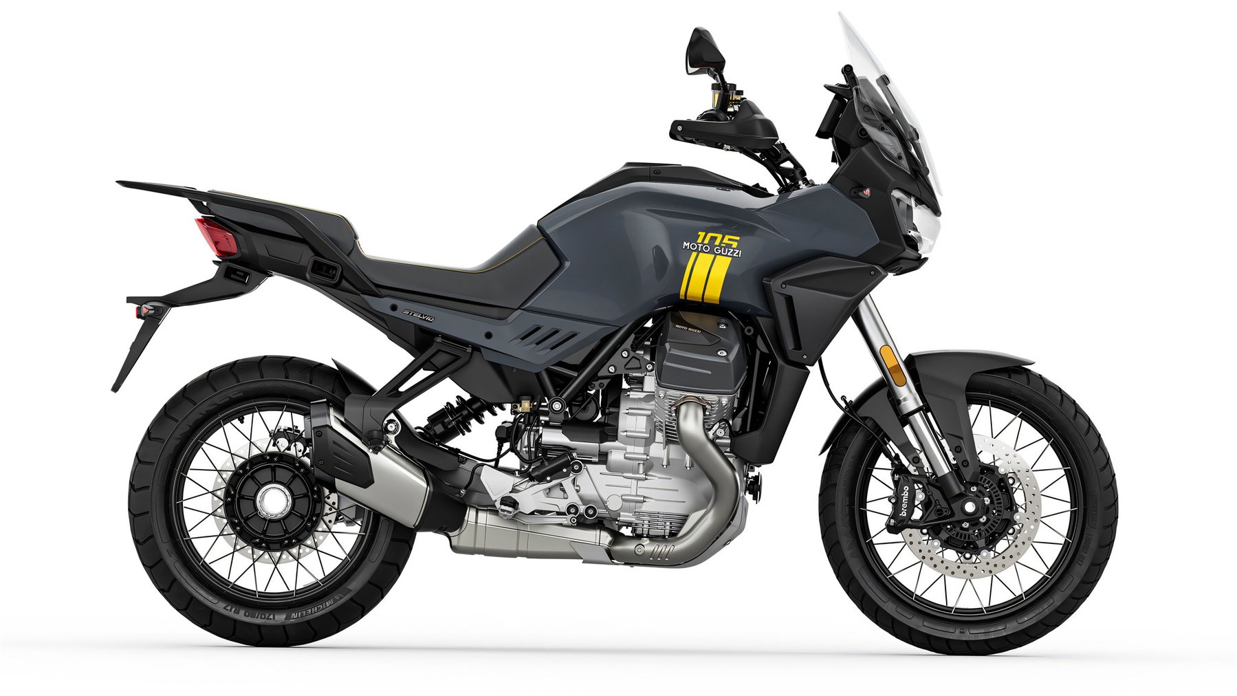Moto Guzzi 105th Anniversary Edition: Fünf Modelle tragen die Farben des neuen Werks 4 Moto Guzzi Stelvio 105th Anniversary Edition – Seitenansicht in Perlglanz-Grau mit gelber „105“-Jubiläumsgrafik am Tank und Speichenrädern, Studioaufnahme vor weißem Hintergrund