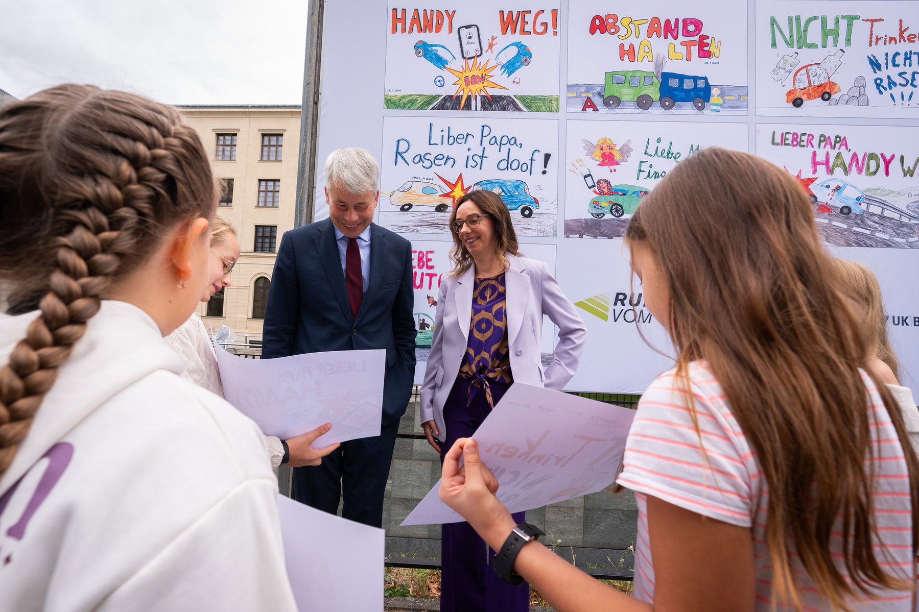 Runter vom Gas: Kinderbilder statt Leichensäcke an der Autobahn 3 Bundesverkehrsminister Steffen Bilger und DVR-Vizepräsidentin Christiane Leonard im Gespräch mit Mädchen, die Ausdrucke ihrer Zeichnungen halten, vor der Plakatwand mit den neuen „Runter vom Gas“-Kinderplakaten in Berlin