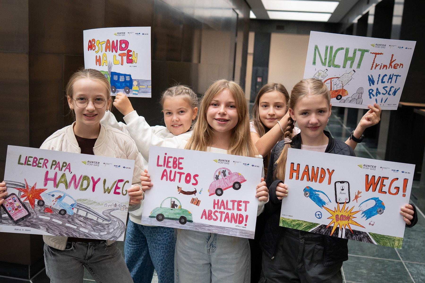 Runter vom Gas: Kinderbilder statt Leichensäcke an der Autobahn 6 Fünf lächelnde Mädchen halten im Foyer des Verkehrsministeriums ihre Plakate „Lieber Papa, Handy weg“, „Abstand halten“, „Liebe Autos, haltet Abstand!“, „Nicht trinken, nicht rasen“ und „Handy weg!“ hoch