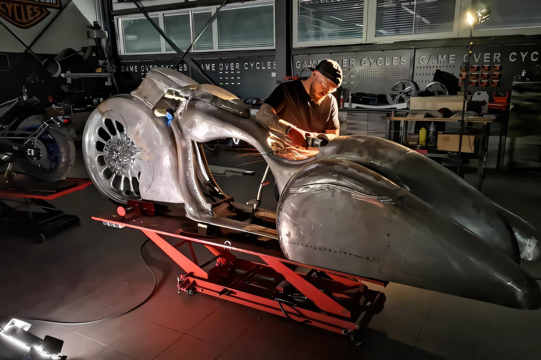 Slow Burn: How Game Over Cycles Turned a 1936 Auburn Into a Bagger 4 Werkstattaufnahme: Der blanke Metallrahmen und Kotfluegel der Slow Burn Bagger im Rohbau auf einer Hebebuehne, ein Mitarbeiter von Game Over Cycles arbeitet daran